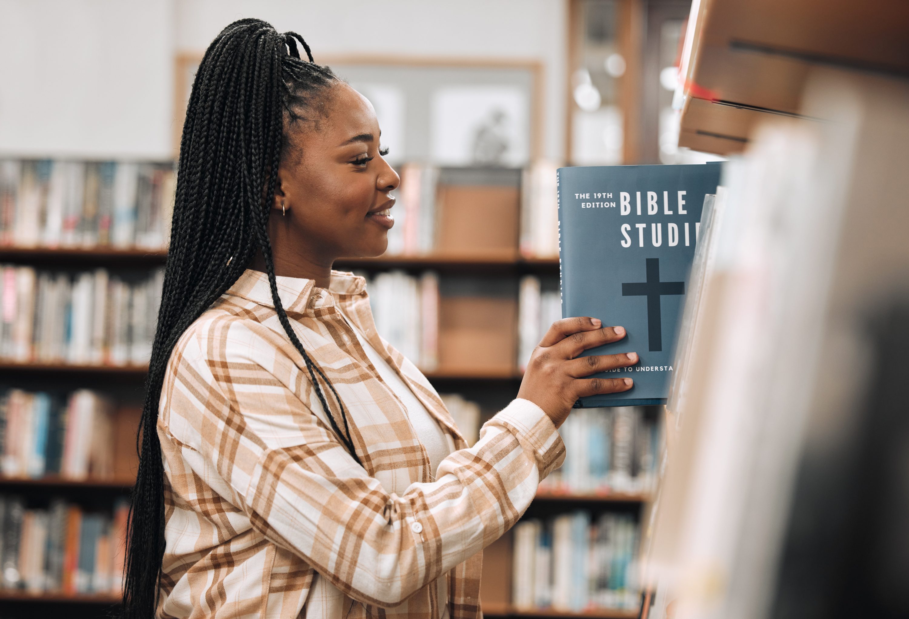 Religion book, education and black woman in a library for research, studying God and knowledge on the bible at college. Learning, smile and African student with decision of books on a scholarship.